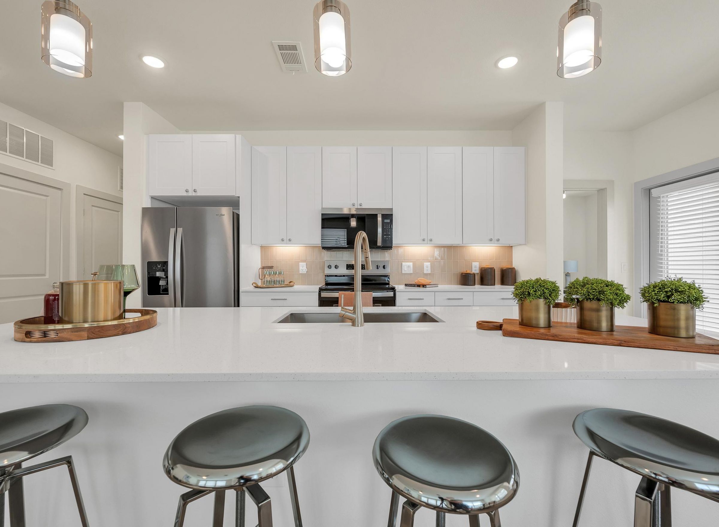 Camber Ridge Modern kitchen with white cabinets, stainless steel appliances, and a large island with stools and decor.