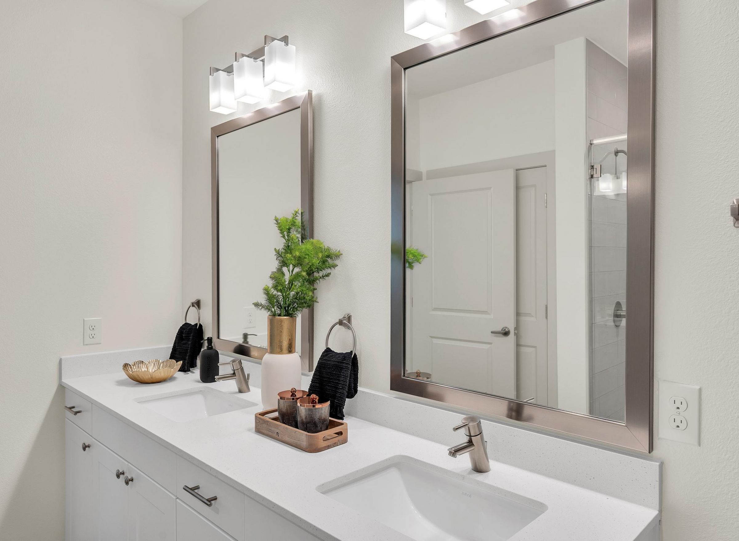 Camber Ridge Modern bathroom with double sinks, rectangular mirrors, and a potted plant. White walls and minimal decor.