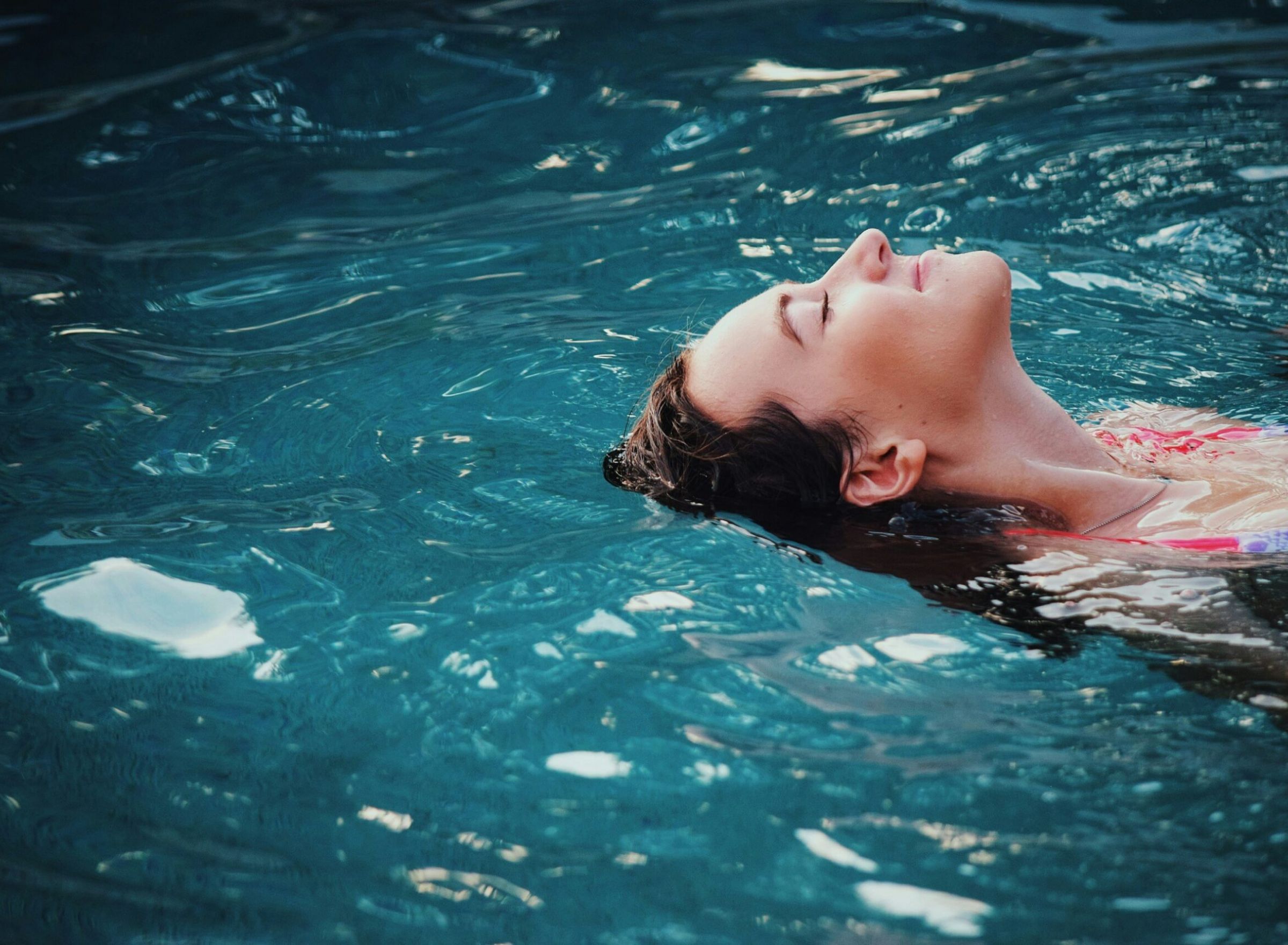 Woman floating peacefully on her back in a blue swimming pool, eyes closed, enjoying the water.