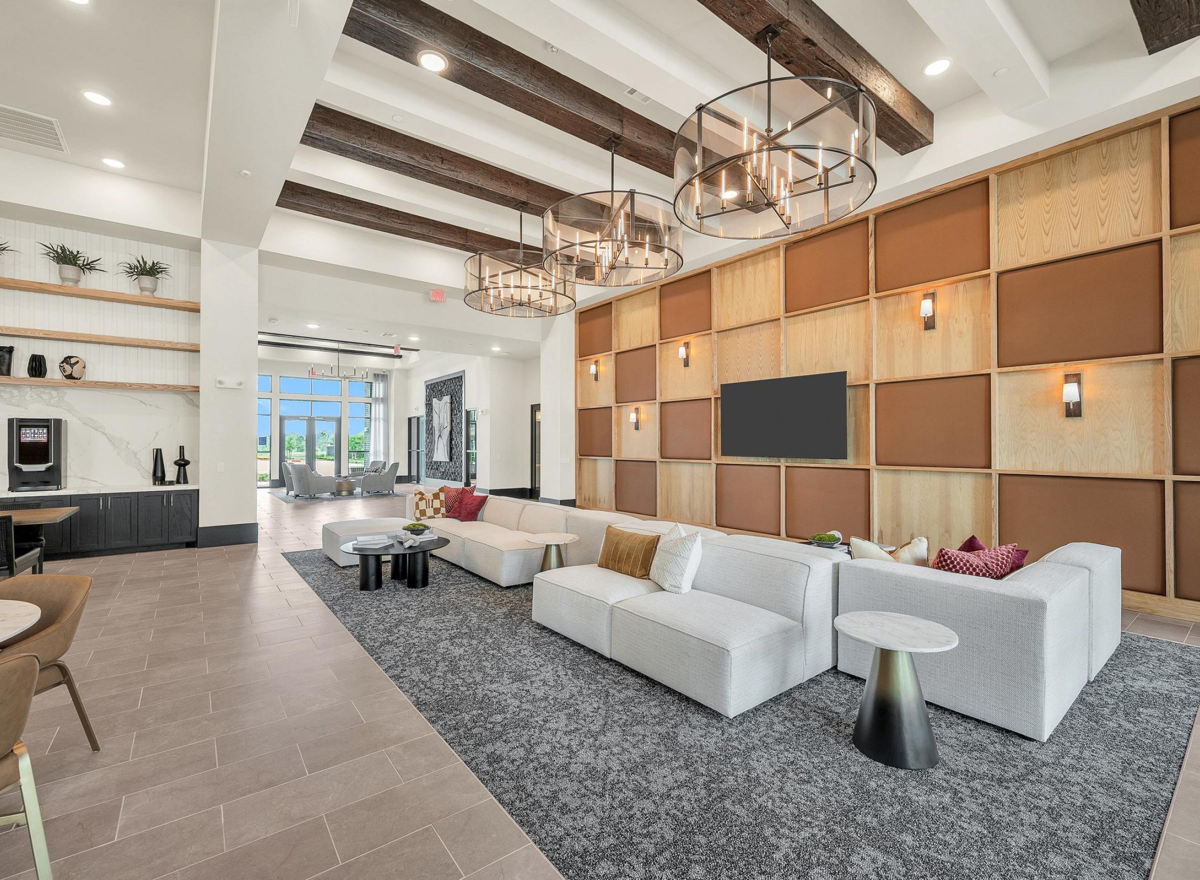 Spacious modern lobby with white sofas, a large TV, wooden beams, and decorative lights.