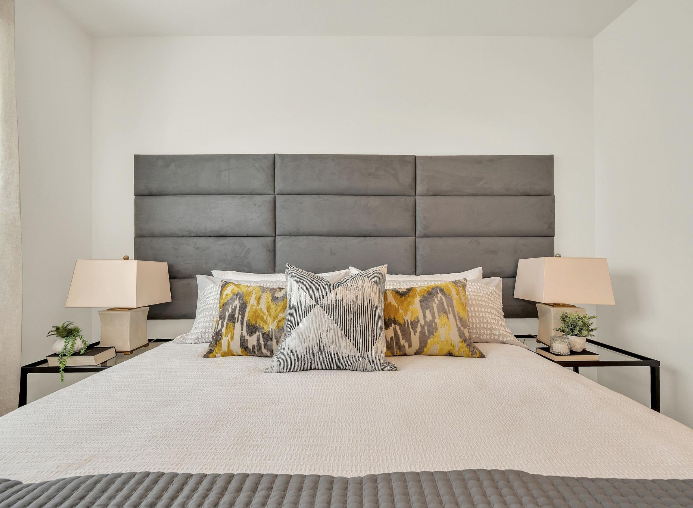 Camber Ridge Modern bedroom with a large gray headboard, abstract pillows, side tables, and stylish lamps.