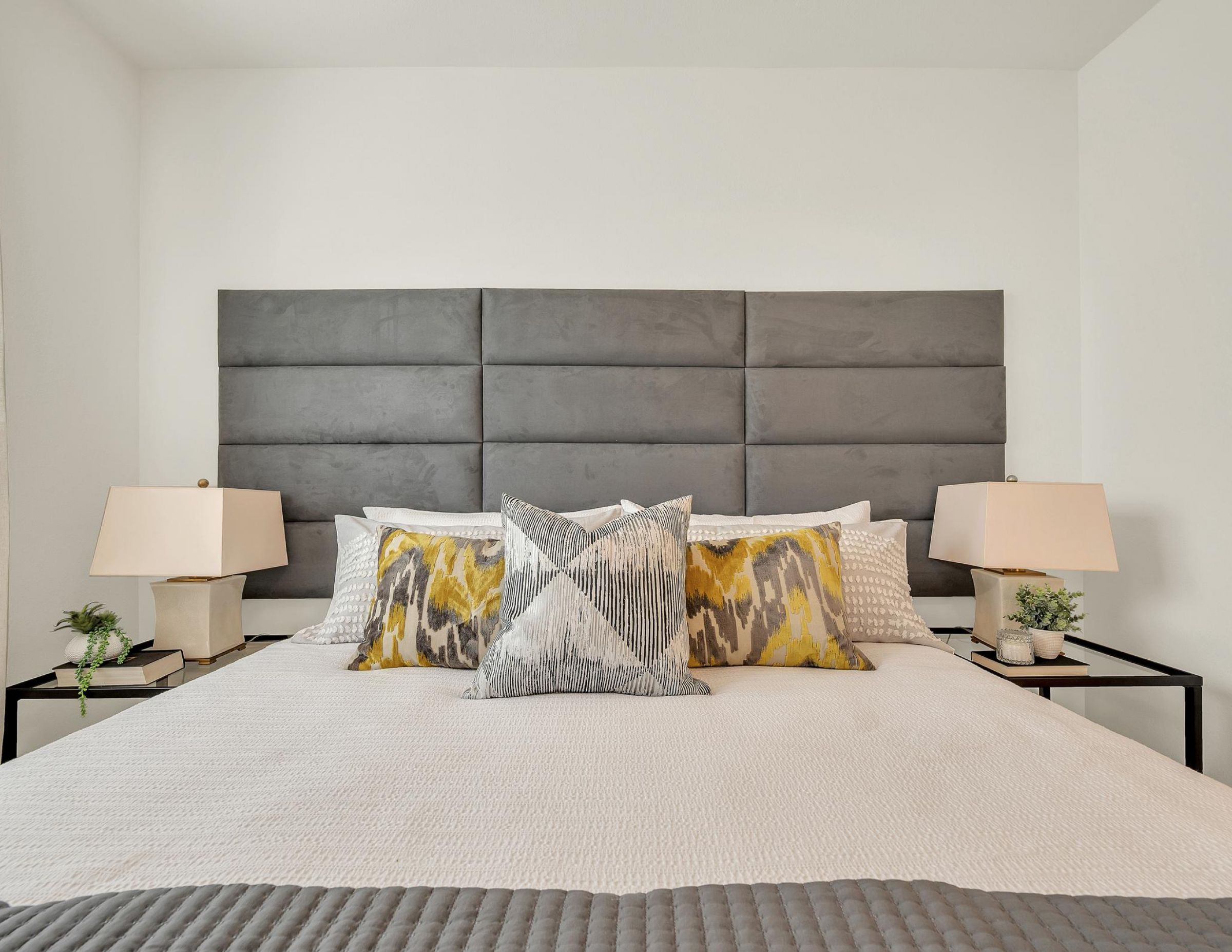 Camber Ridge Modern bedroom with a large gray headboard, abstract pillows, side tables, and stylish lamps.