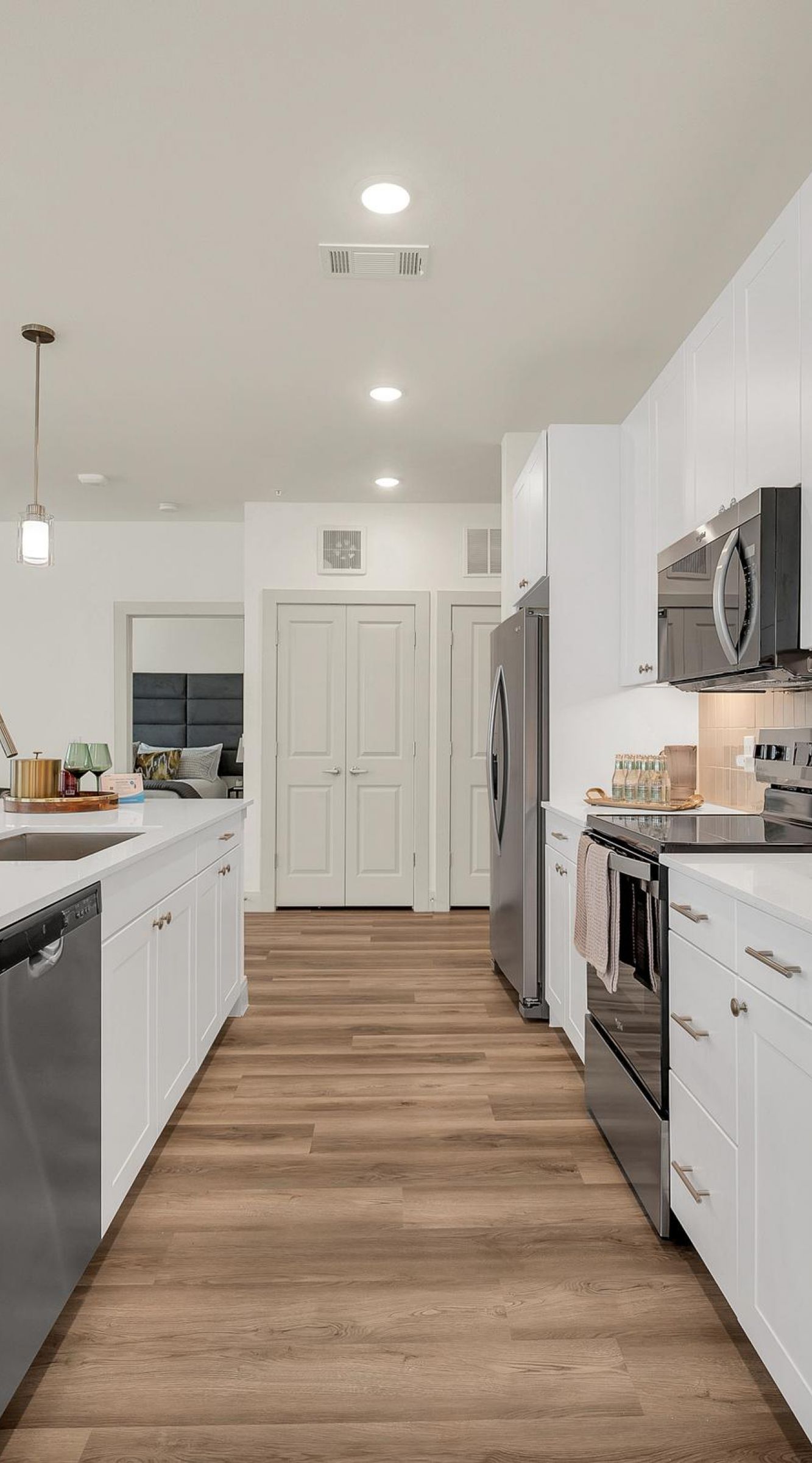 Camber Ridge Modern kitchen with white cabinets, stainless steel appliances, pendant lights, and wooden flooring.