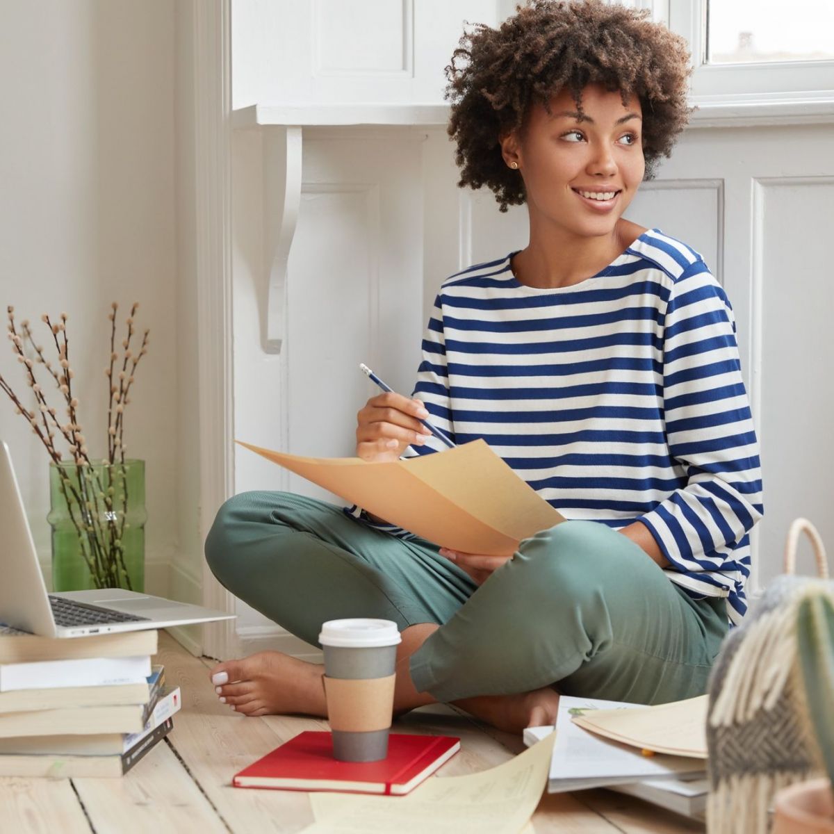 Camber Ridge Woman sits on floor with papers, laptop, and coffee, looking to the side, smiling. Casual, cozy home setting.