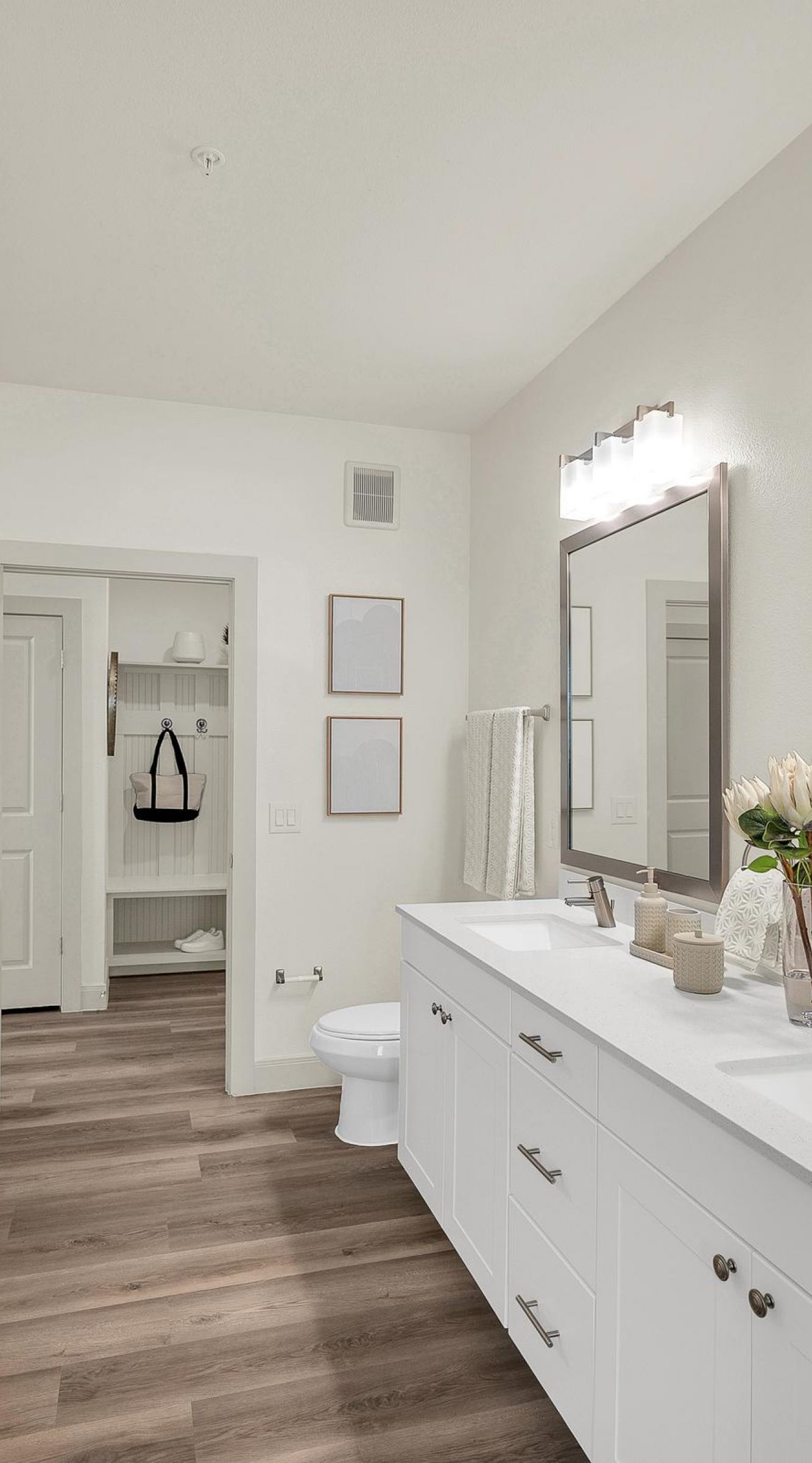 Camber Ridge Modern white bathroom with dual sinks, large mirrors, and wood flooring. Shower, toilet, and storage area visible.