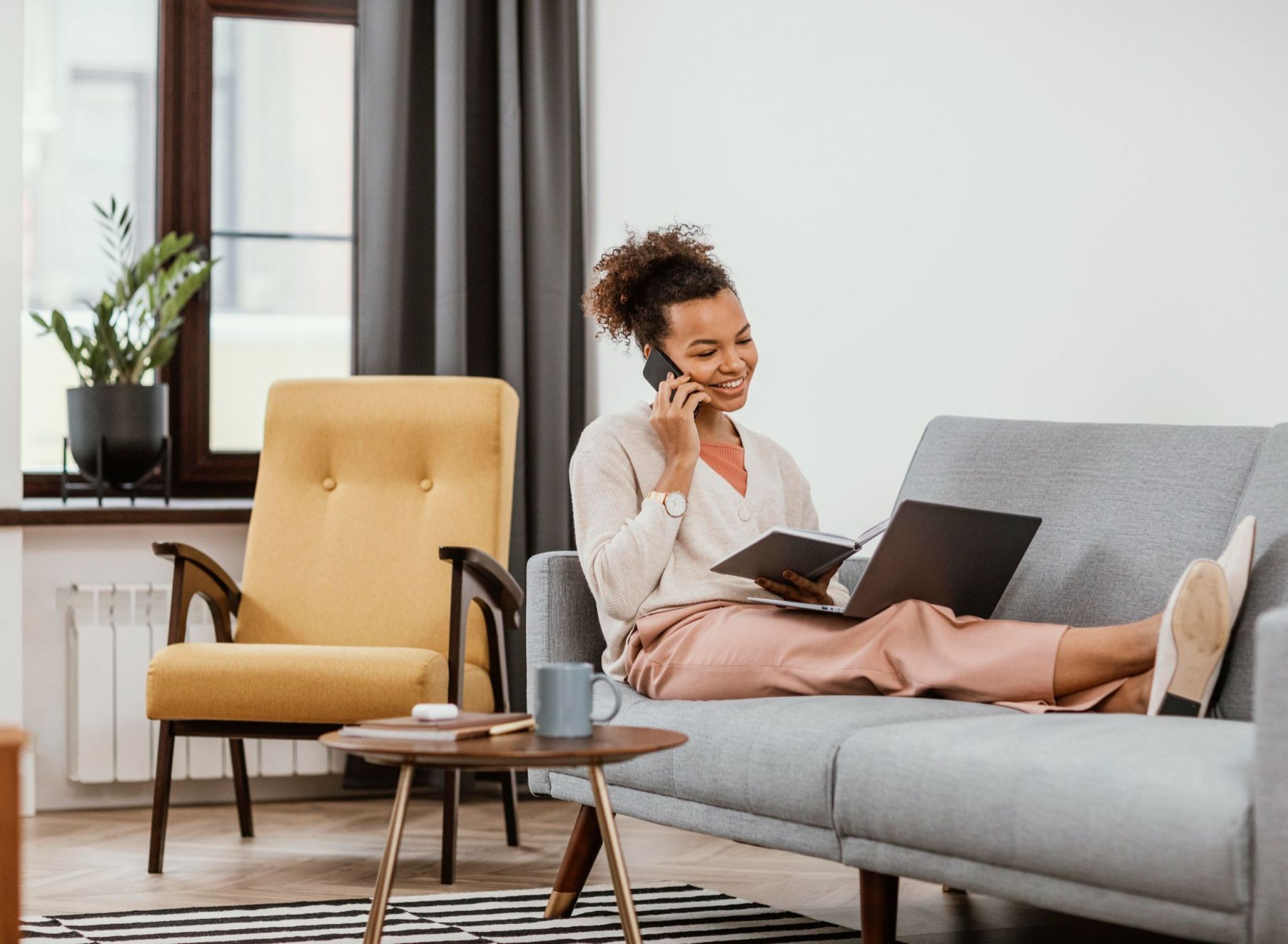 Camber Ridge Smiling woman sits on a couch with a laptop, talking on the phone and holding a tablet.