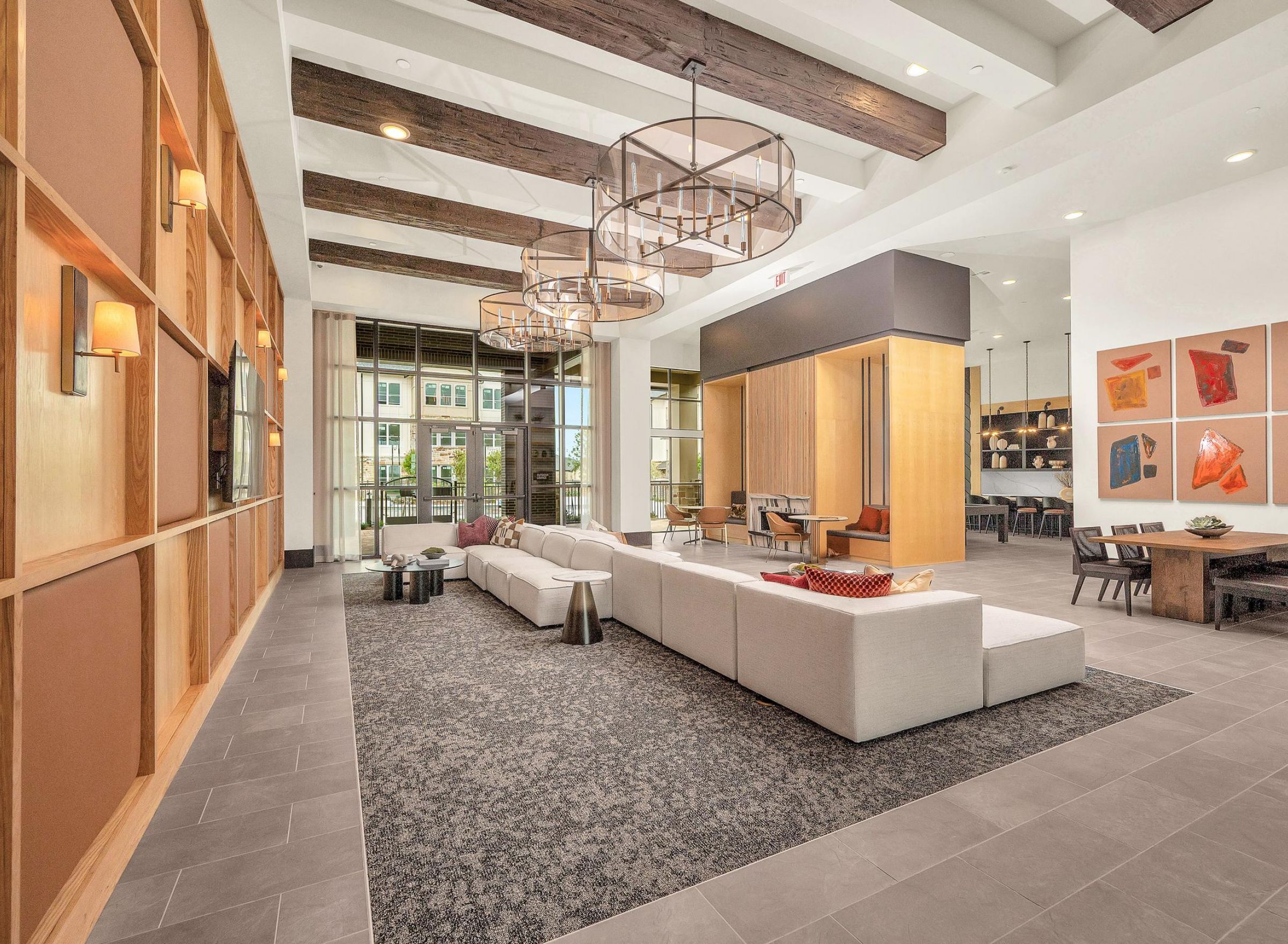 Camber Ridge Modern lounge with red sofas, wooden chairs, and a lattice ceiling featuring globe lights. Large windows let in natural light.